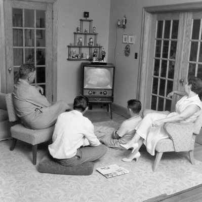 A 1950s black and white photo of a family sitting in front of an early television set